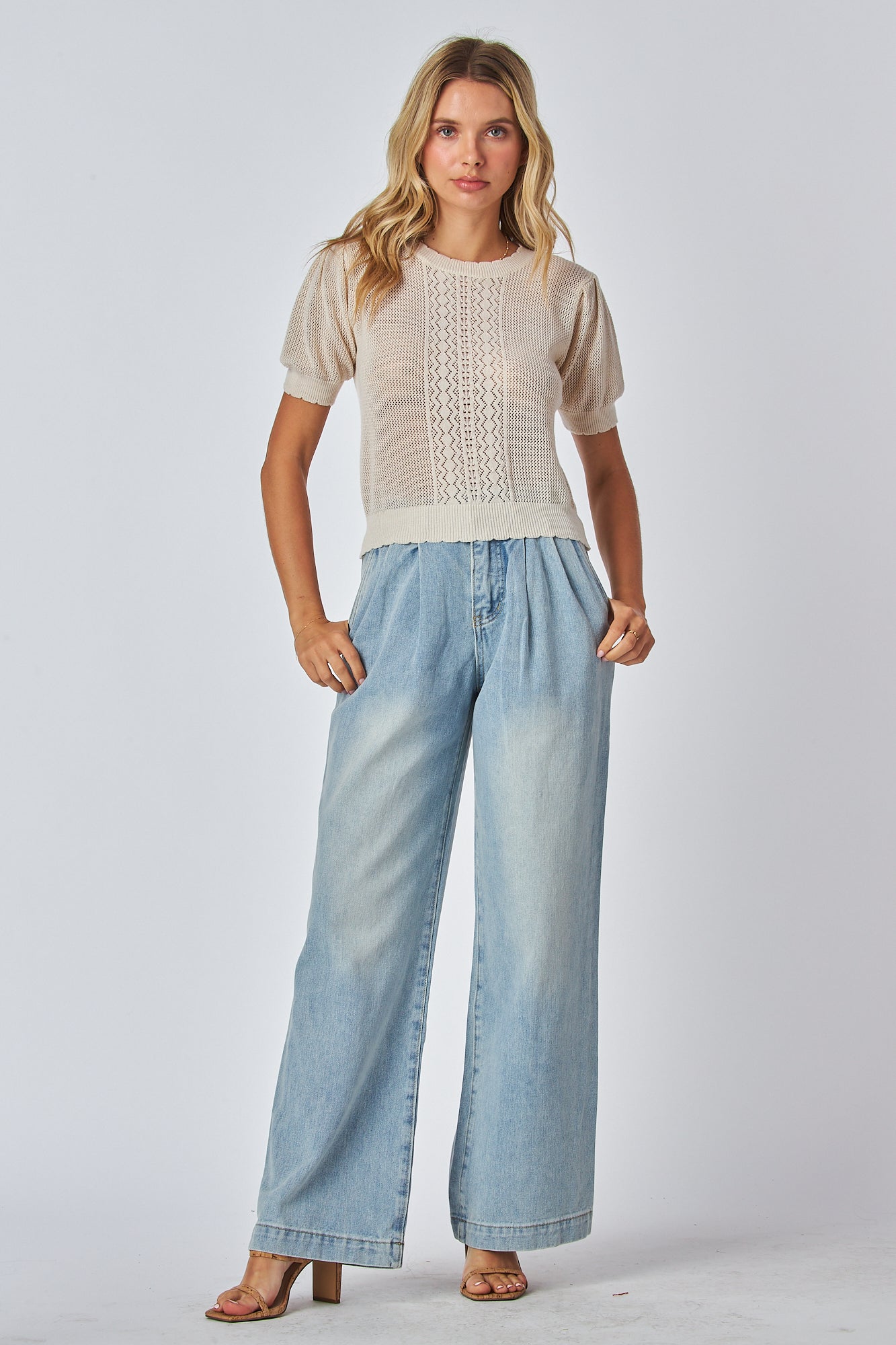 A female model wearing a wide-leg blue denim jeans with a high waist and pleated front.