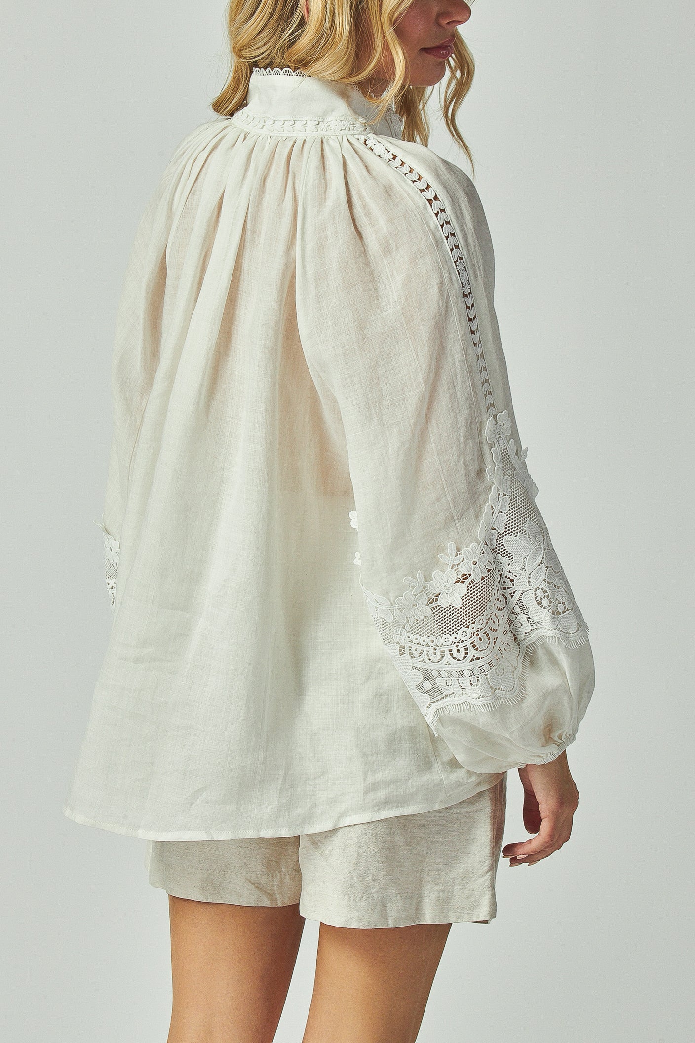 Model wearing a white blouse with lace details on a plain background