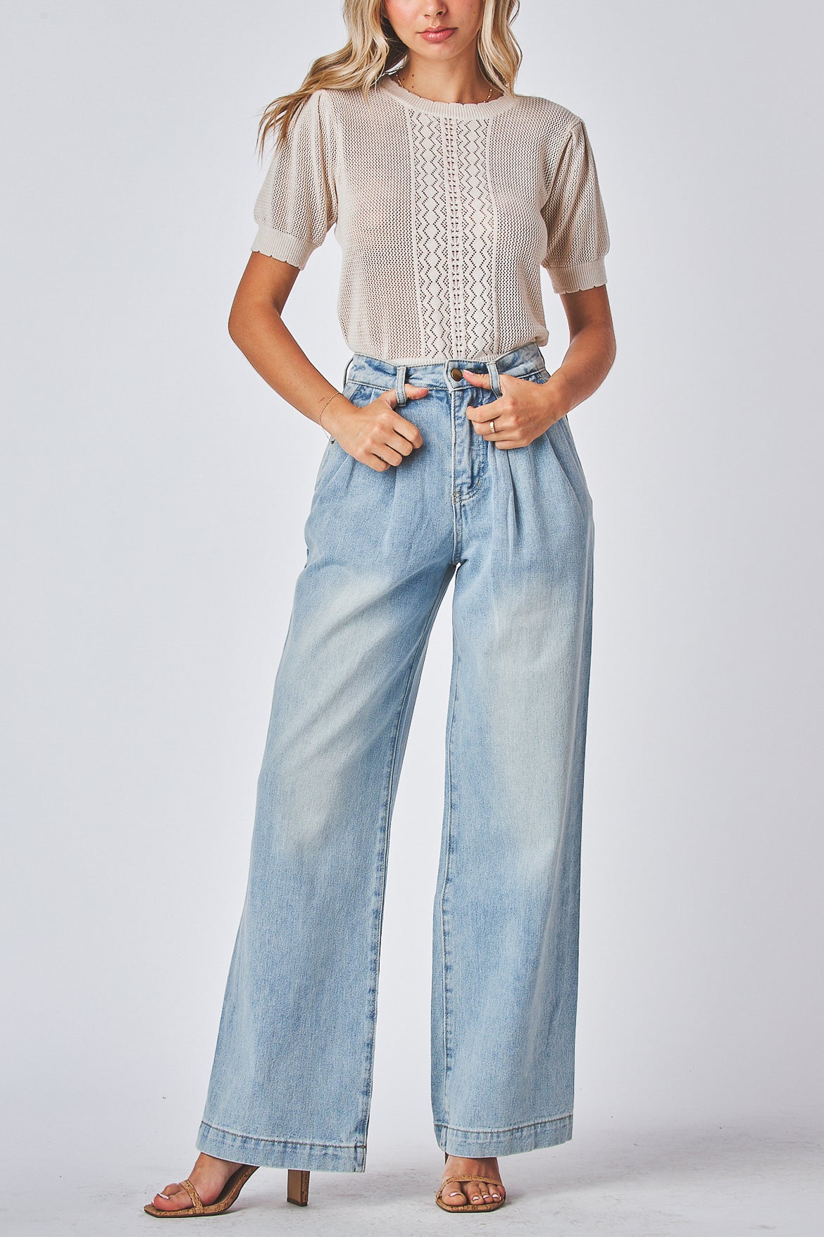 Model wearing a beige top and light blue jeans on a white background