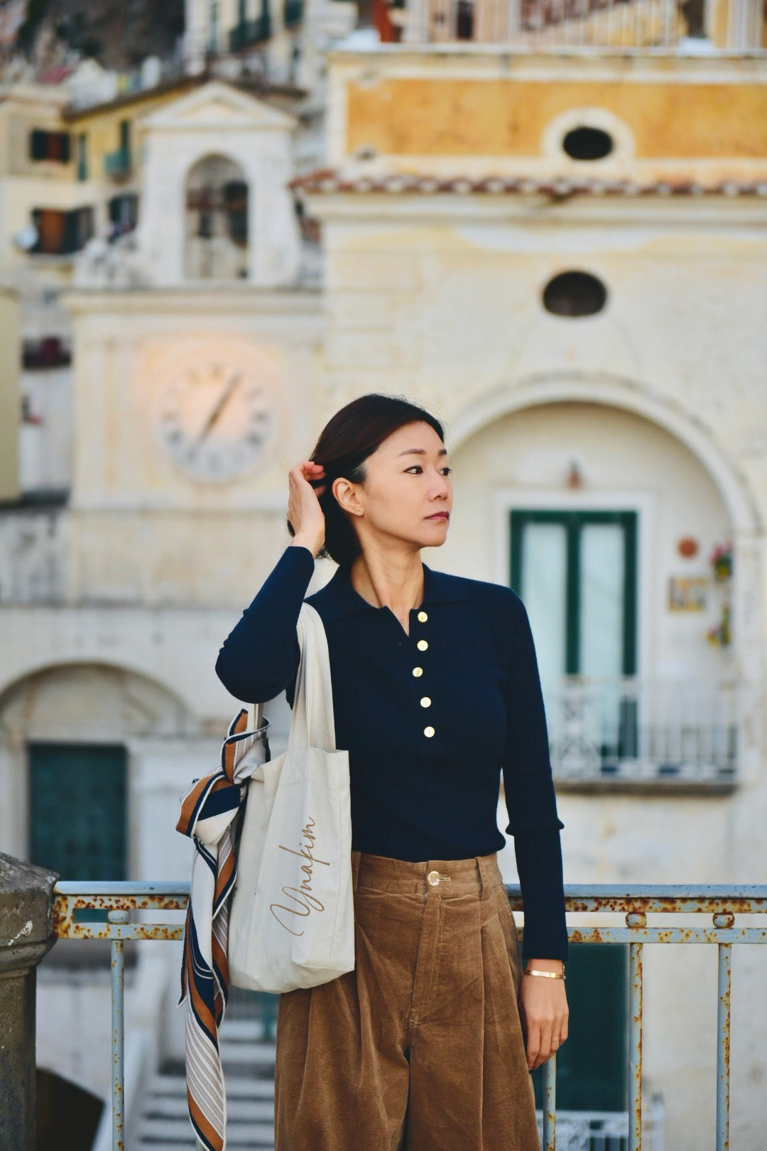 Woman wearing a camel ribbed knit polo sweater with gold buttons and long sleeves, styled with high-waisted blue jeans.