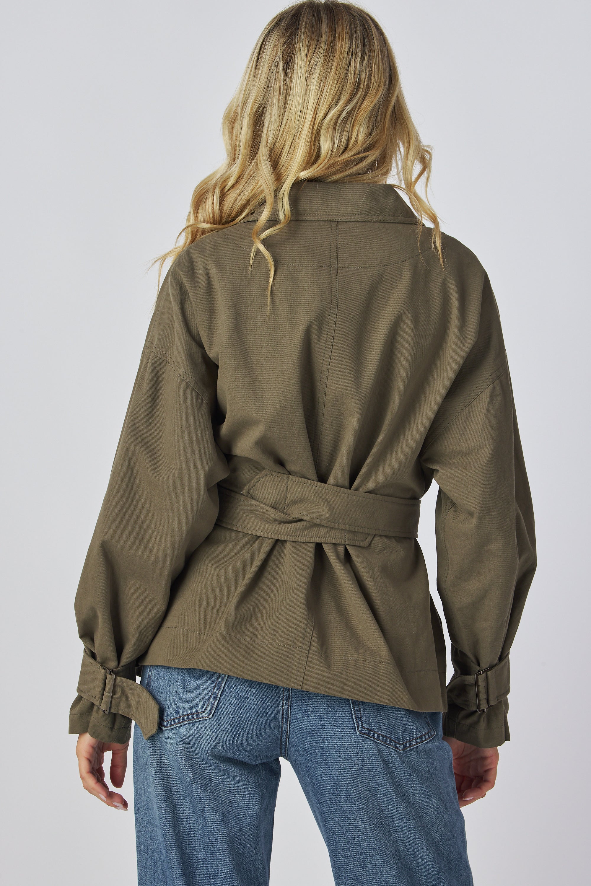 Model wearing a green jacket and blue jeans on a plain background