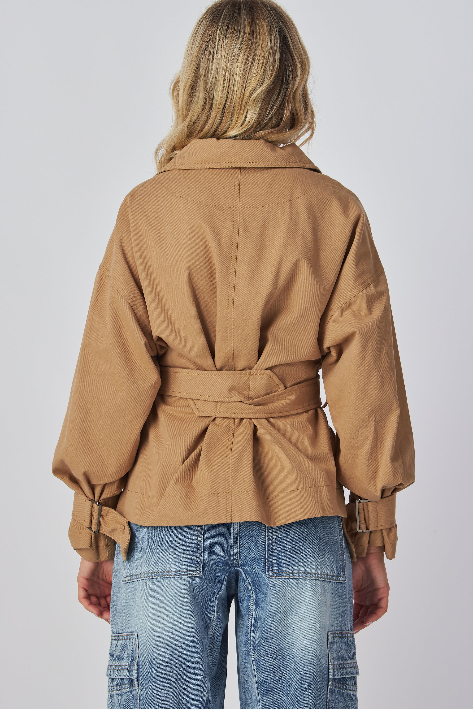 Model wearing a tan jacket and blue jeans on a plain background