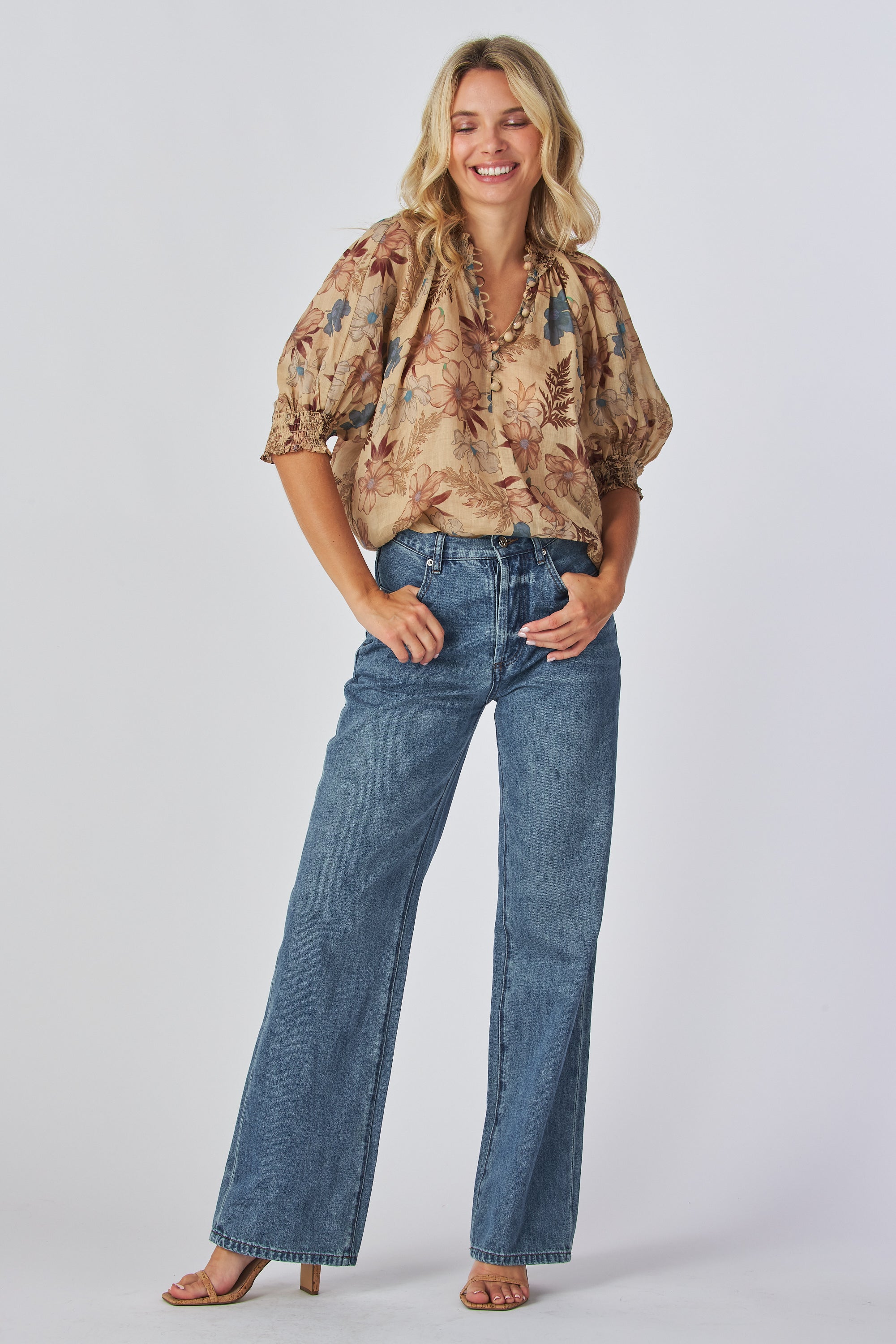 jeans are a classic high-waisted, straight-leg style in a medium blue wash. The fabric has a slightly vintage, lived-in look with subtle fading around the button fly and hip area, giving it a naturally worn effect without heavy distressing. High-rise fit with belt loops,