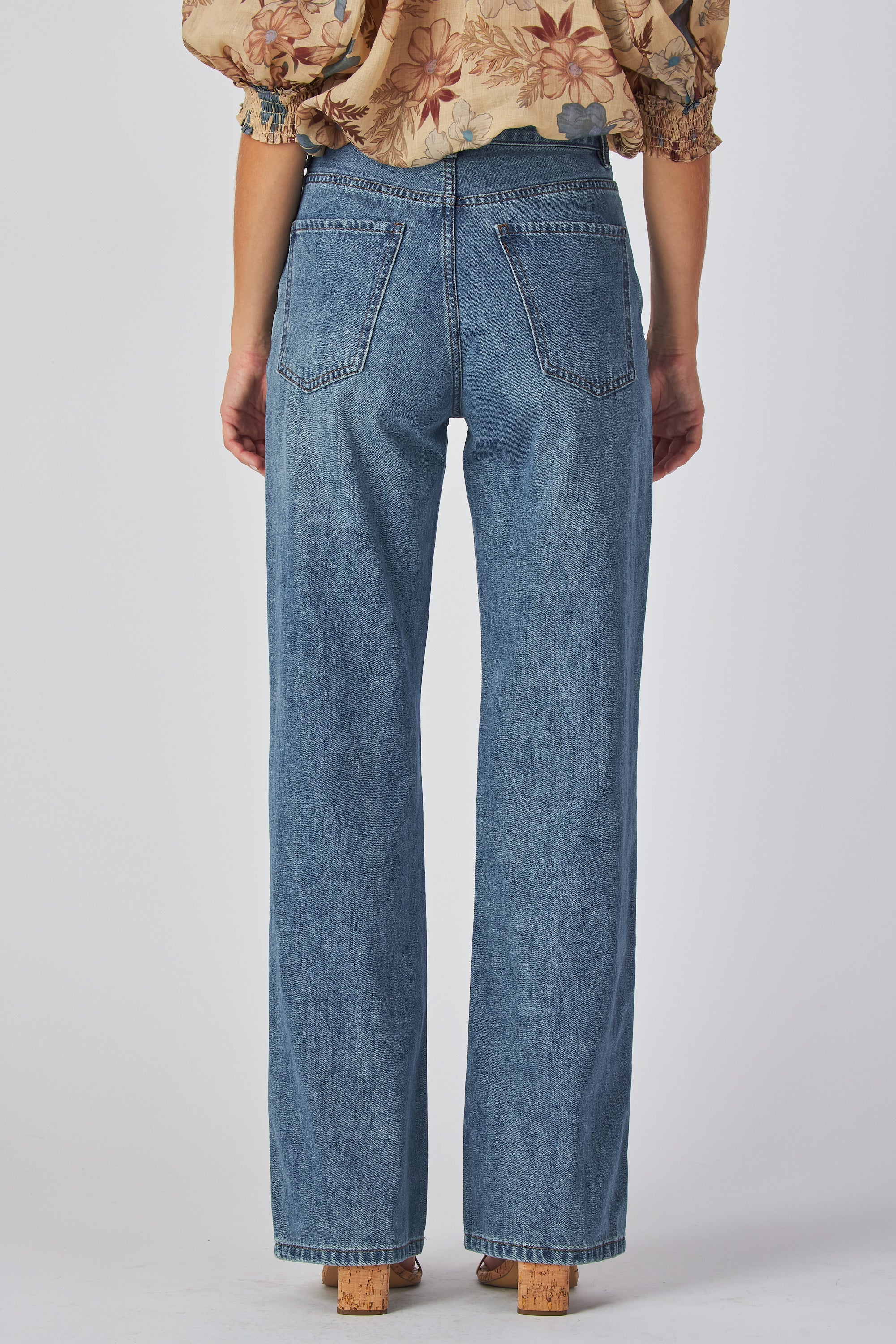 jeans are a classic high-waisted, straight-leg style in a medium blue wash. The fabric has a slightly vintage, lived-in look with subtle fading around the button fly and hip area, giving it a naturally worn effect without heavy distressing. High-rise fit with belt loops,