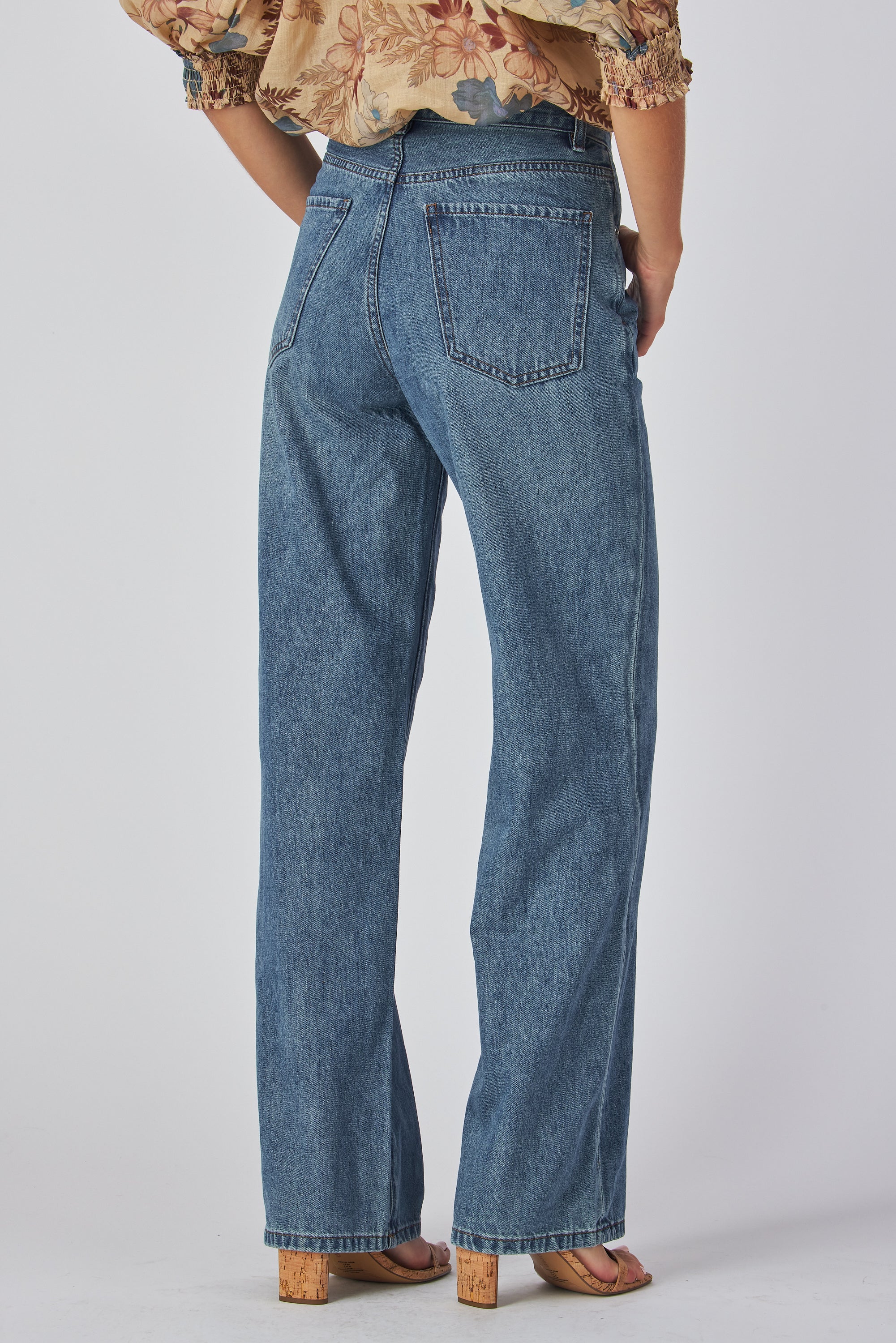 jeans are a classic high-waisted, straight-leg style in a medium blue wash. The fabric has a slightly vintage, lived-in look with subtle fading around the button fly and hip area, giving it a naturally worn effect without heavy distressing. High-rise fit with belt loops,