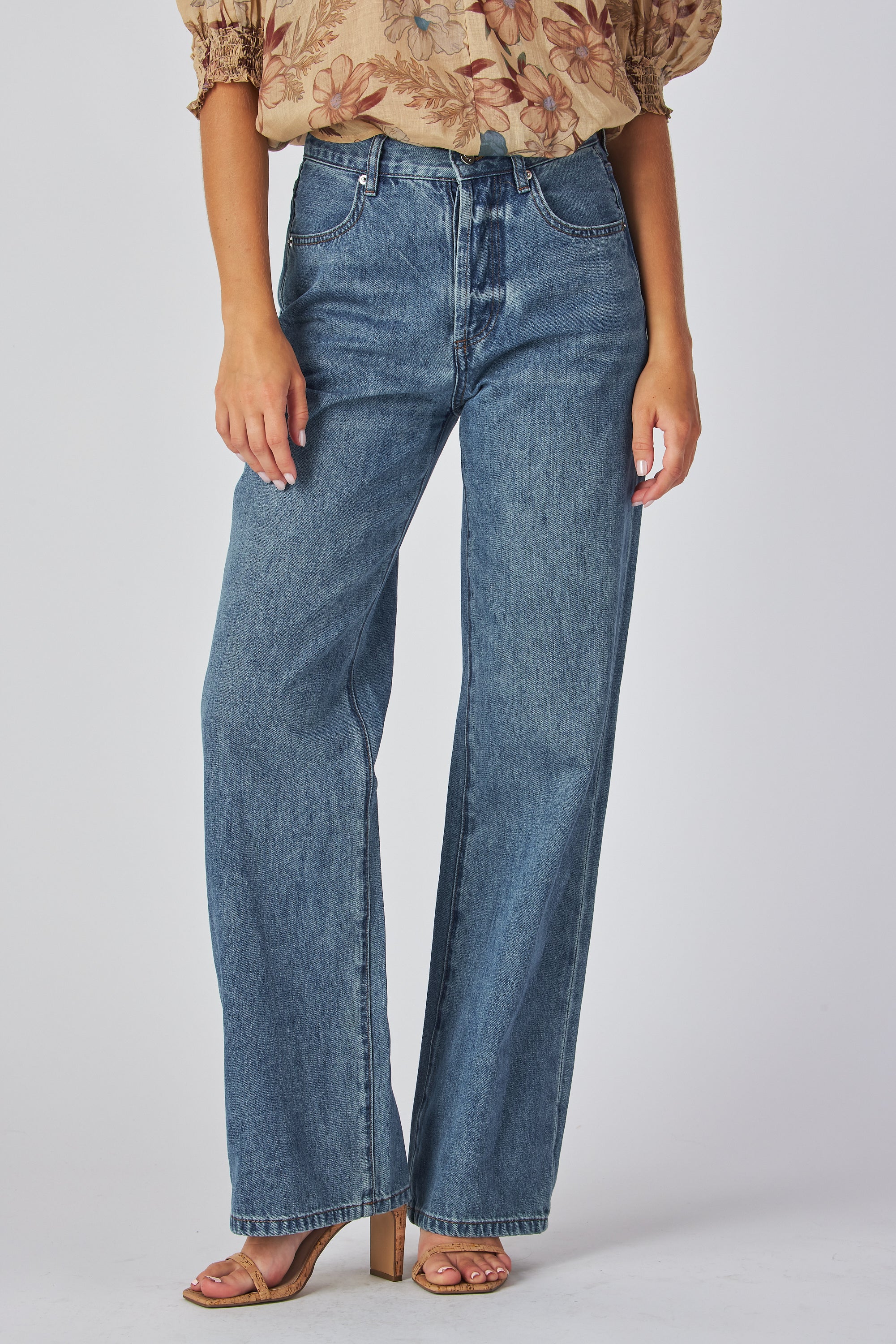 jeans are a classic high-waisted, straight-leg style in a medium blue wash. The fabric has a slightly vintage, lived-in look with subtle fading around the button fly and hip area, giving it a naturally worn effect without heavy distressing. High-rise fit with belt loops,