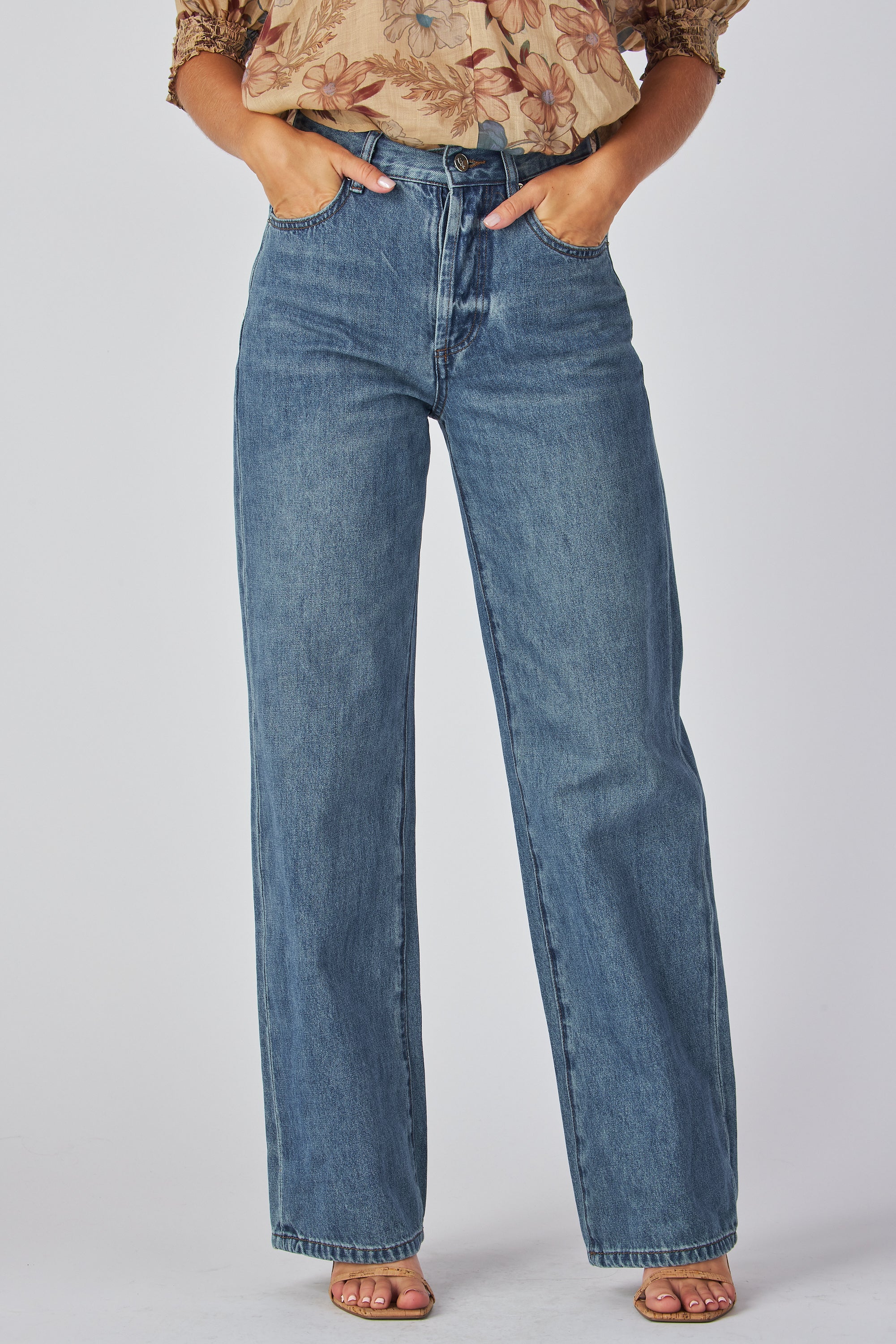 jeans are a classic high-waisted, straight-leg style in a medium blue wash. The fabric has a slightly vintage, lived-in look with subtle fading around the button fly and hip area, giving it a naturally worn effect without heavy distressing. High-rise fit with belt loops,