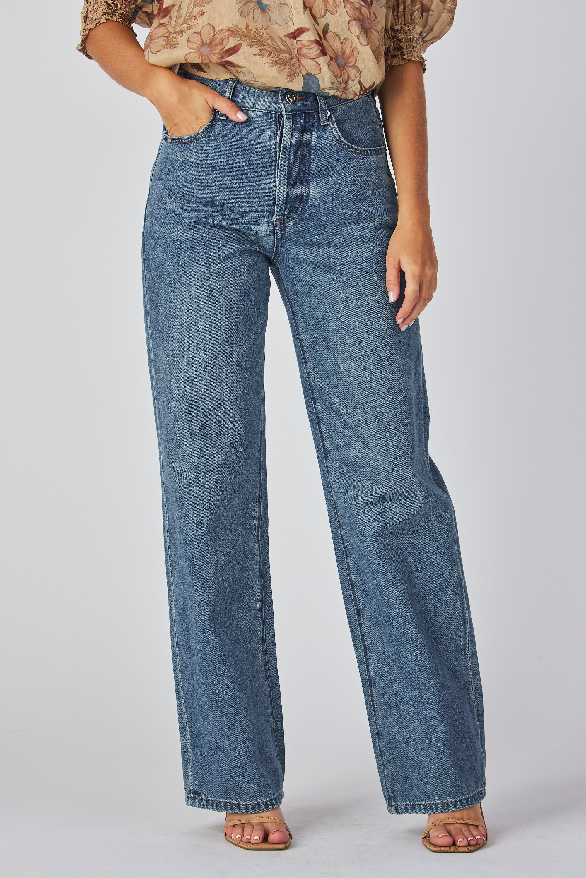 jeans are a classic high-waisted, straight-leg style in a medium blue wash. The fabric has a slightly vintage, lived-in look with subtle fading around the button fly and hip area, giving it a naturally worn effect without heavy distressing. High-rise fit with belt loops,