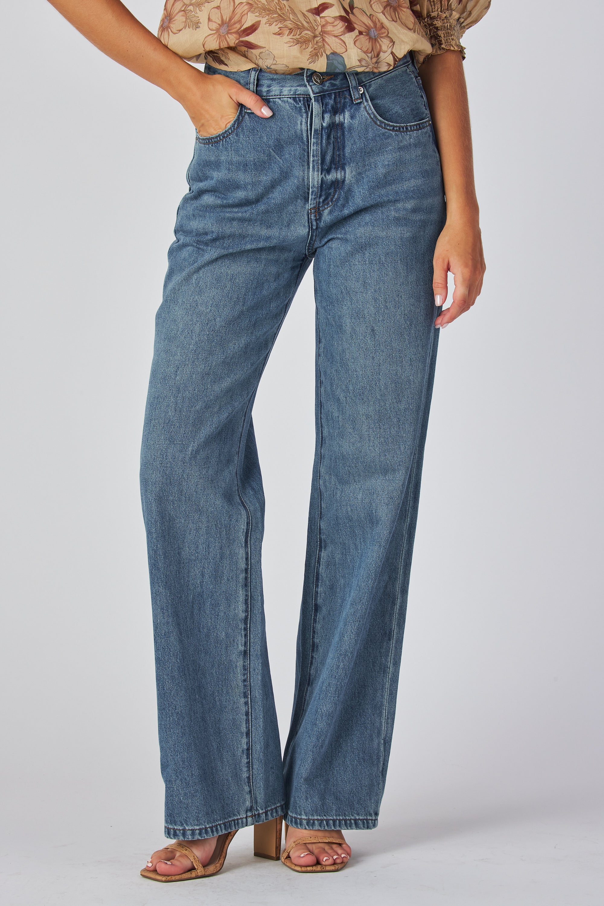 jeans are a classic high-waisted, straight-leg style in a medium blue wash. The fabric has a slightly vintage, lived-in look with subtle fading around the button fly and hip area, giving it a naturally worn effect without heavy distressing. High-rise fit with belt loops,