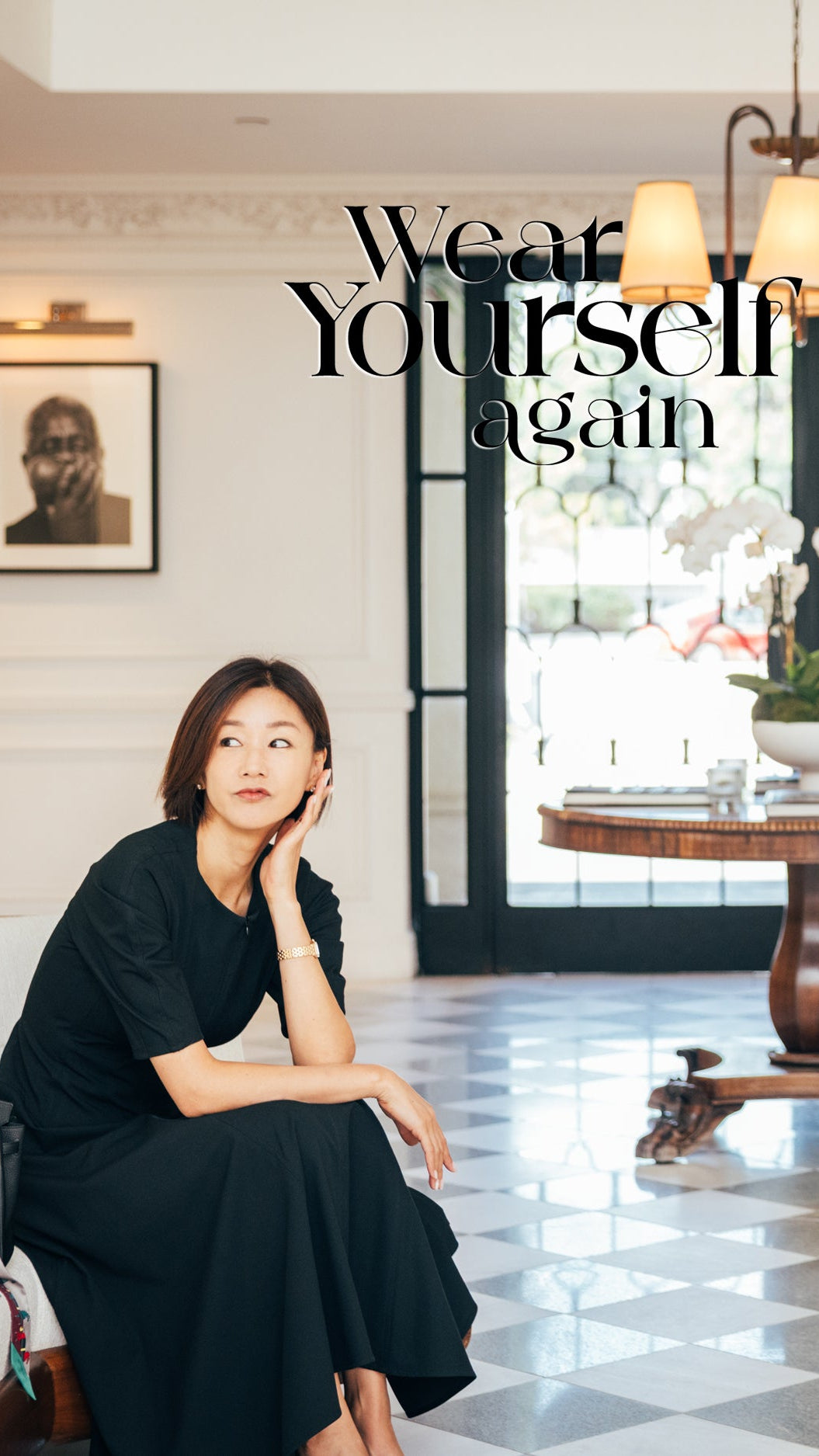 Woman in a black dress sitting in a stylish room with text 'Wear Yourself Again'.