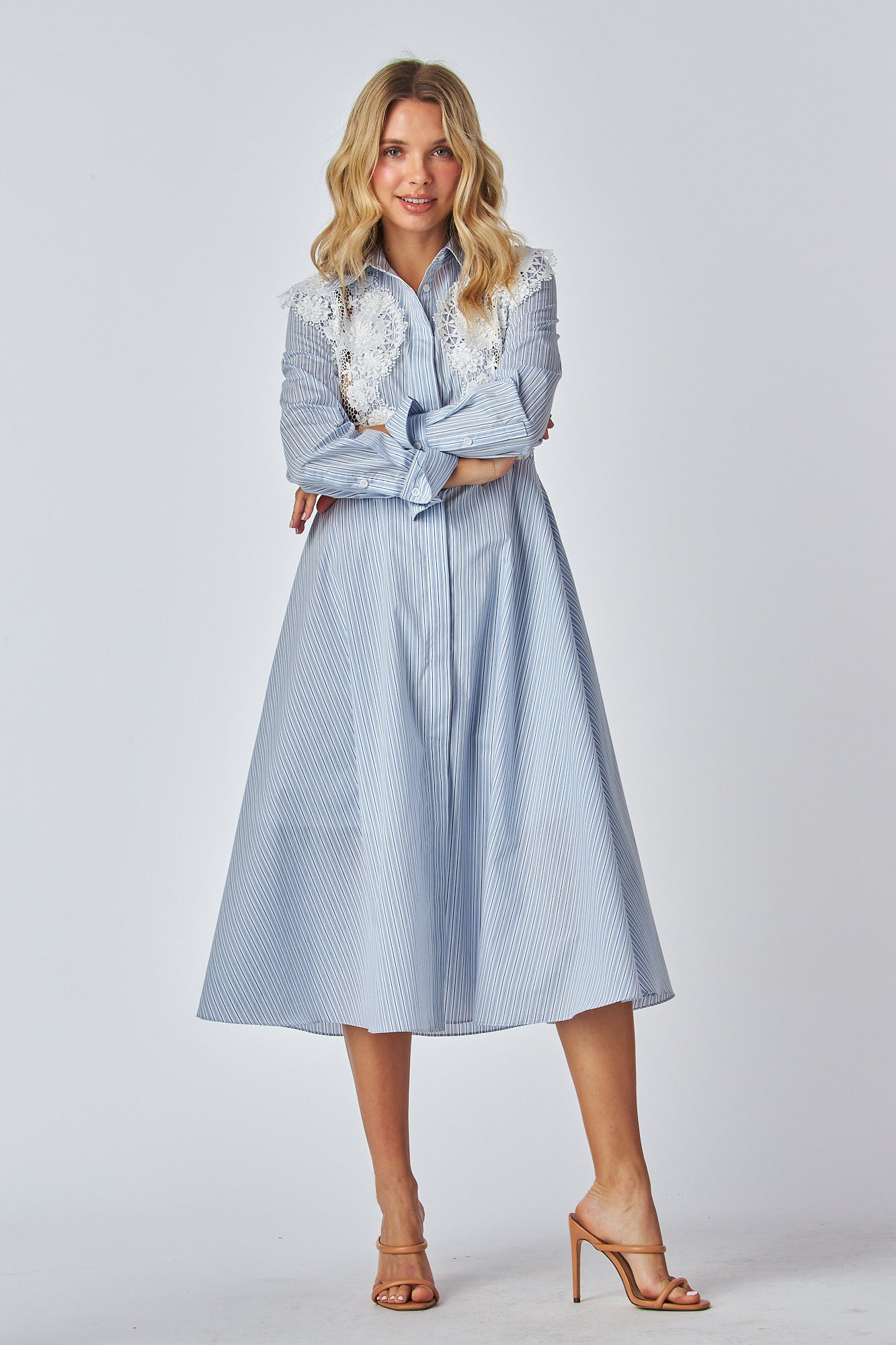 Model in a light blue and white striped shirt dress with a traditional collar and long sleeves, featuring white lace applique on the chest area. The dress has a flared A-line silhouette and is midi-length.