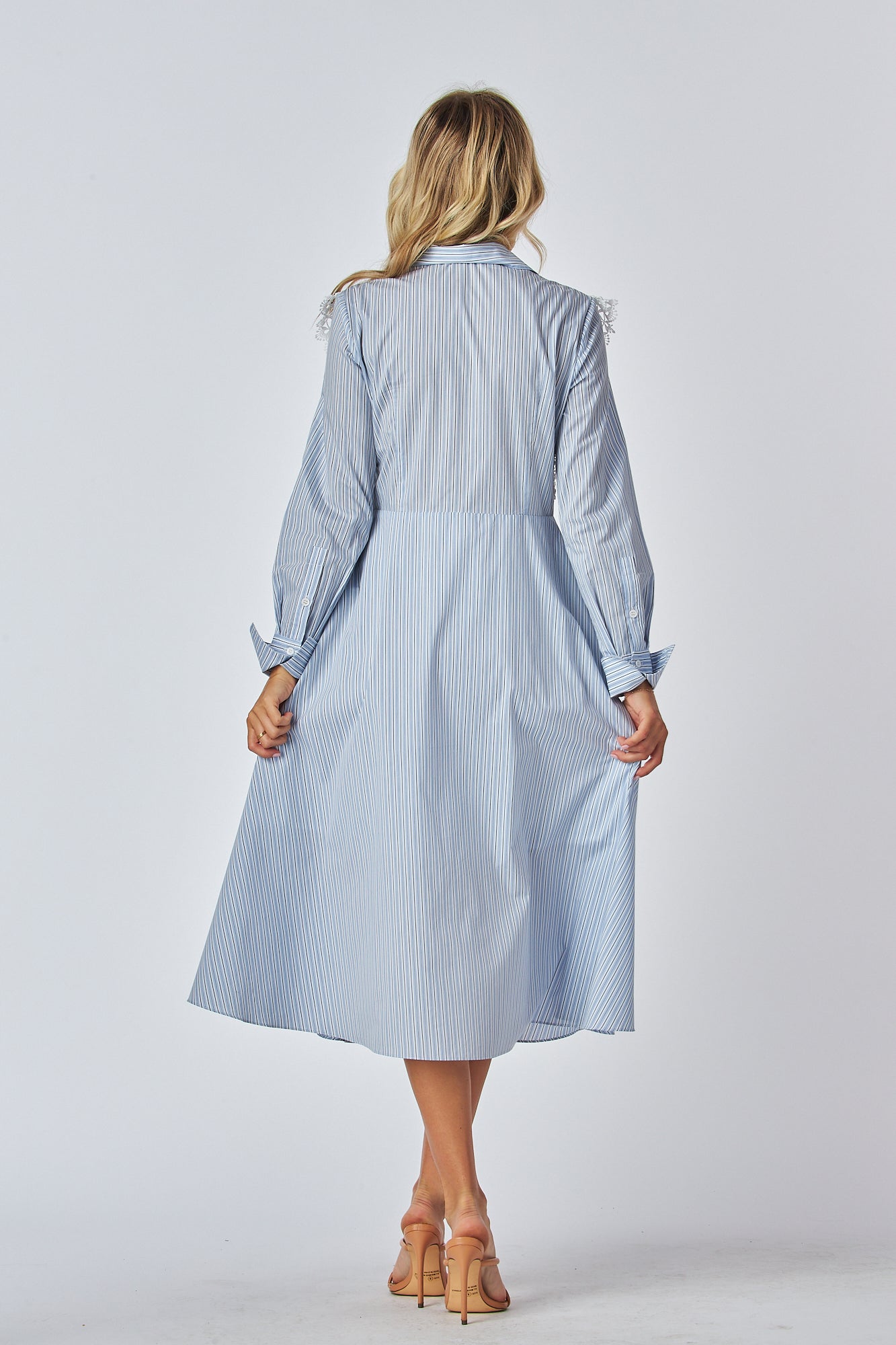 Model in a light blue and white striped shirt dress with a traditional collar and long sleeves, featuring white lace applique on the chest area. The dress has a flared A-line silhouette and is midi-length.