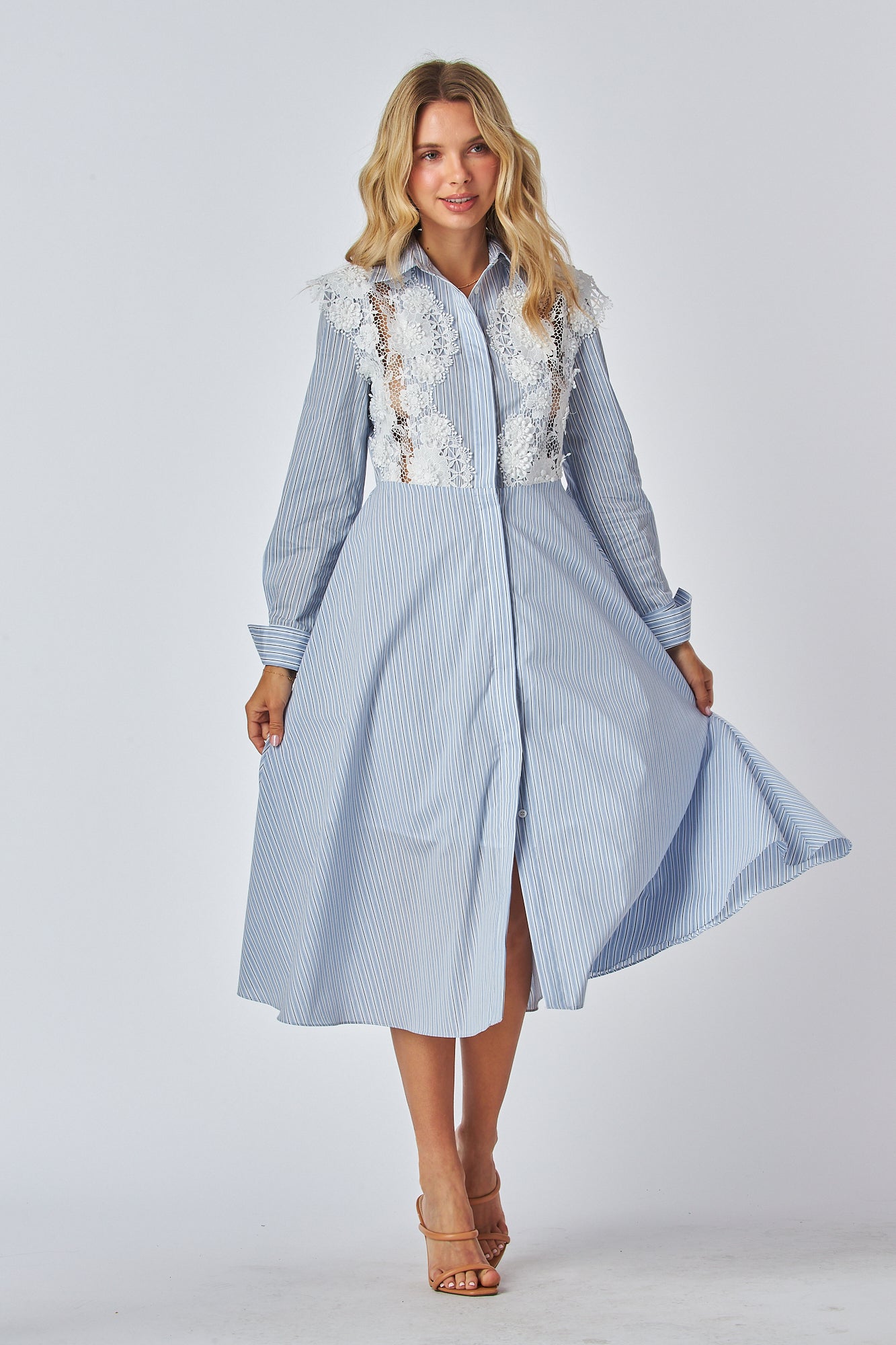 Model in a light blue and white striped shirt dress with a traditional collar and long sleeves, featuring white lace applique on the chest area. The dress has a flared A-line silhouette and is midi-length.
