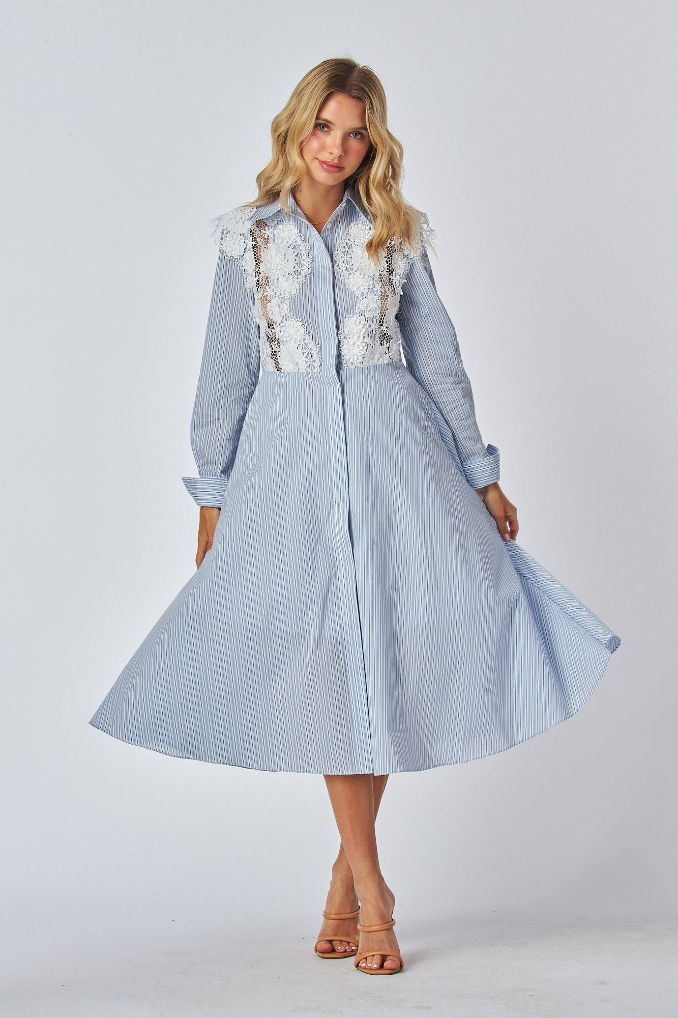 Model in a light blue and white striped shirt dress with a traditional collar and long sleeves, featuring white lace applique on the chest area. The dress has a flared A-line silhouette and is midi-length.