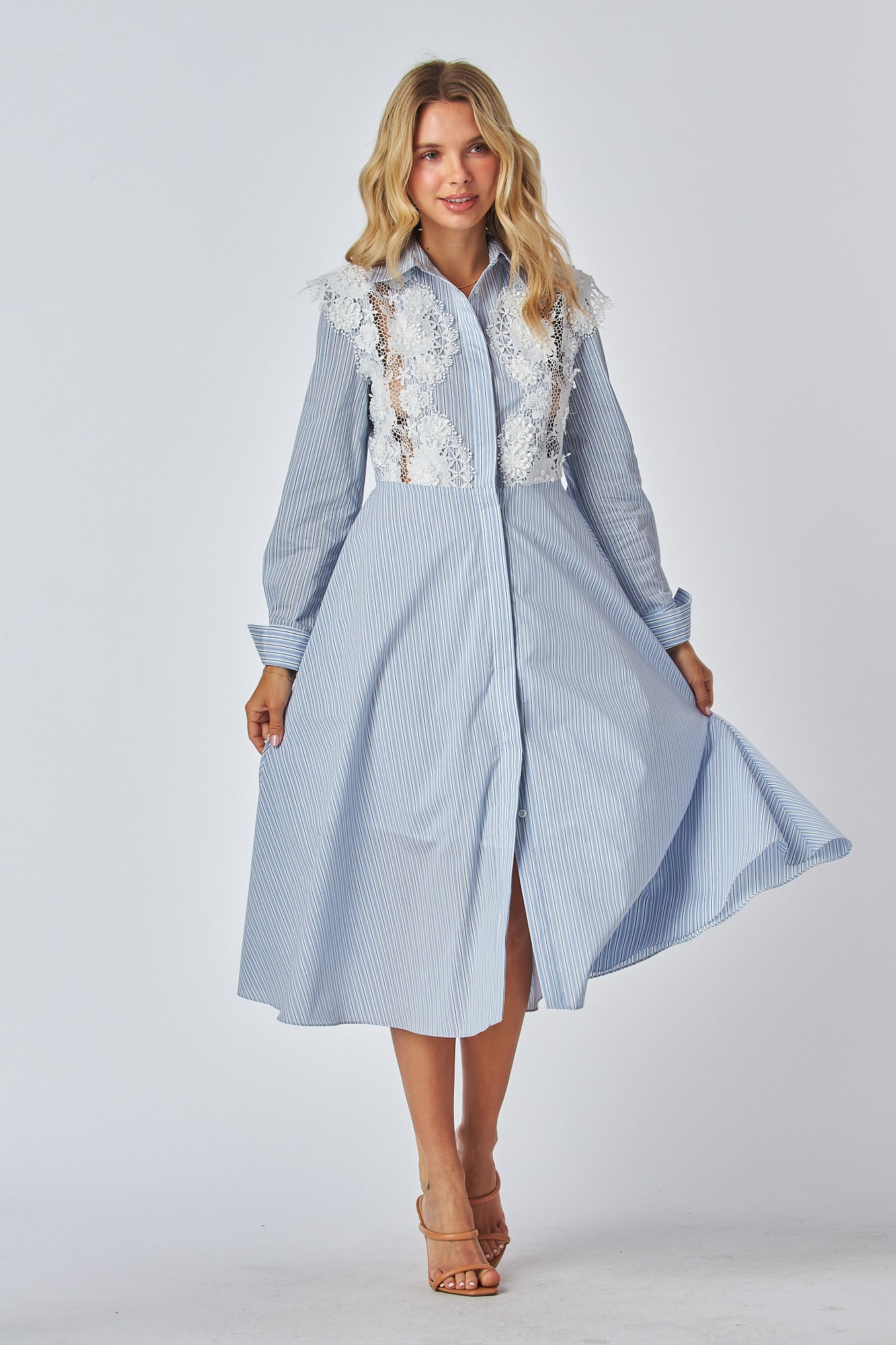 Model in a light blue and white striped shirt dress with a traditional collar and long sleeves, featuring white lace applique on the chest area. The dress has a flared A-line silhouette and is midi-length.