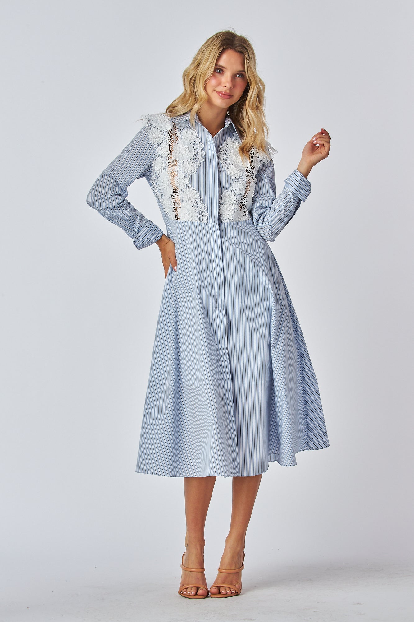 Model in a light blue and white striped shirt dress with a traditional collar and long sleeves, featuring white lace applique on the chest area. The dress has a flared A-line silhouette and is midi-length.