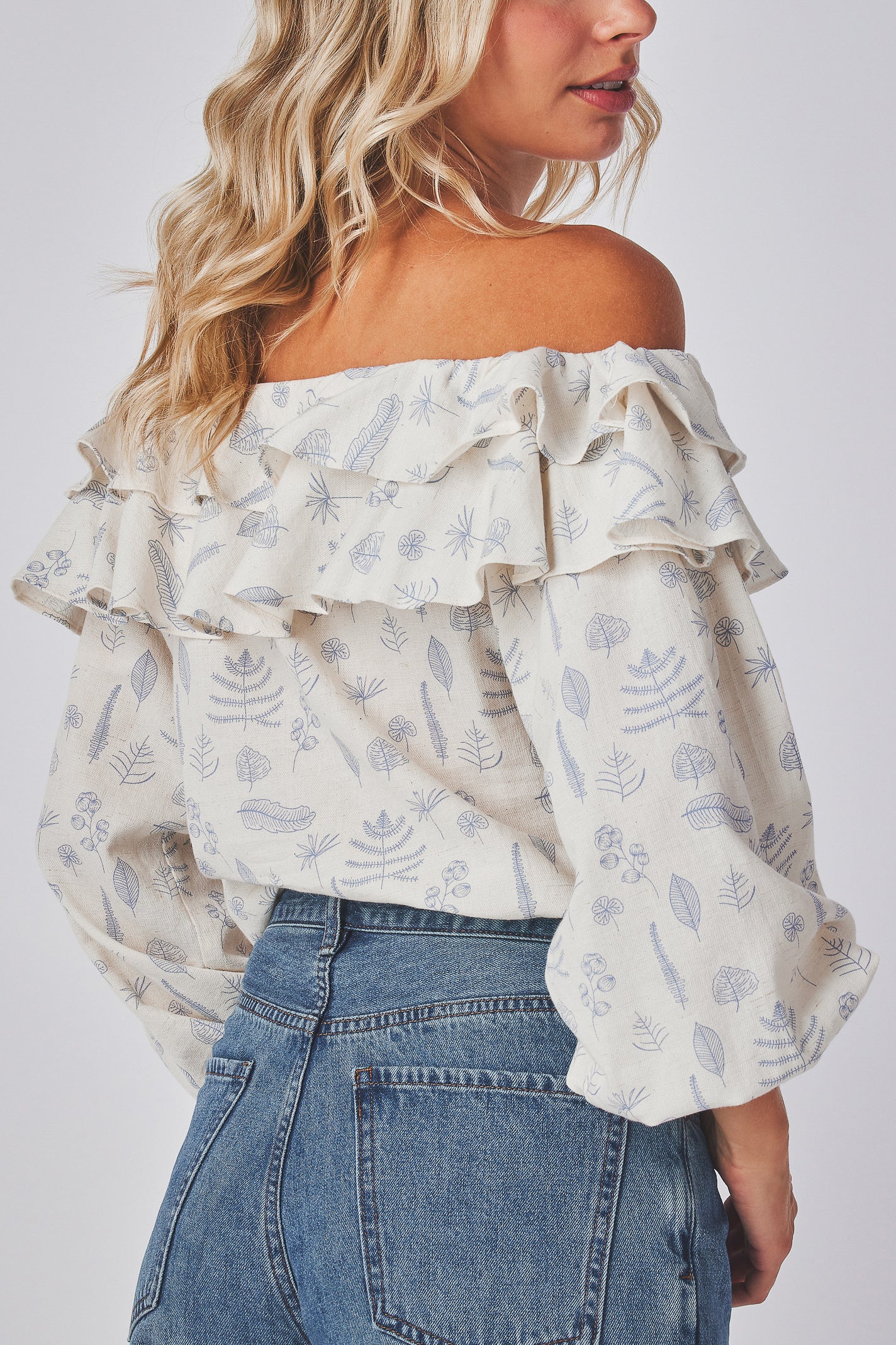 Model wearing a floral off-shoulder top and blue jeans on a white background