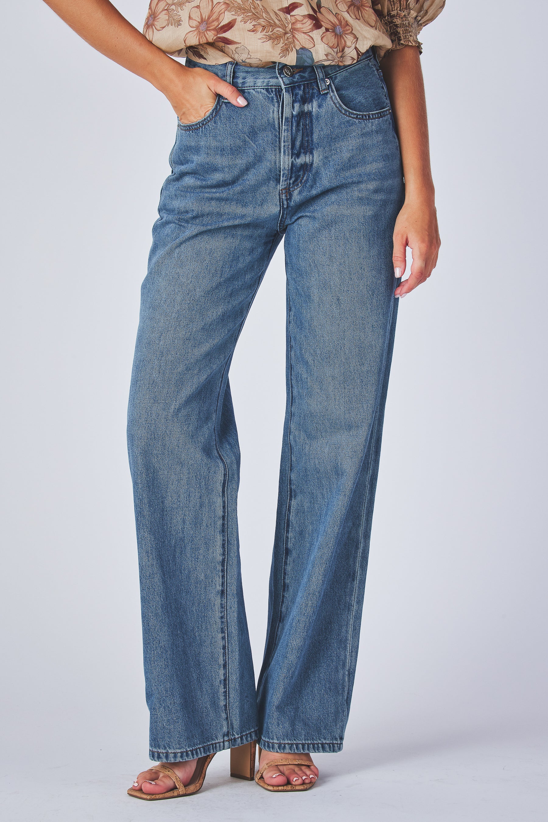 jeans are a classic high-waisted, straight-leg style in a medium blue wash. The fabric has a slightly vintage, lived-in look with subtle fading around the button fly and hip area, giving it a naturally worn effect without heavy distressing. High-rise fit with belt loops,