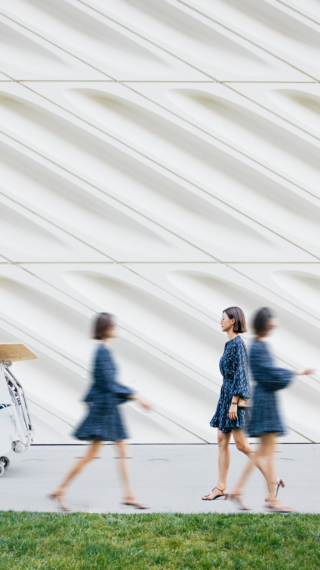 Two women walking past a modern architectural structure with a robot in the foreground.
